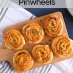 Wooden serving board holding hot ham and cheese pinwheels, surrounded by plates. Text overlay includes recipe name.