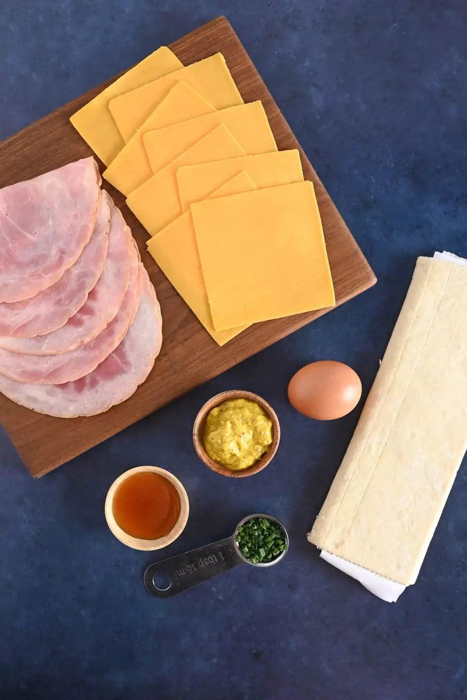 Ingredients for hot ham and cheese pinwheels arranged on a blue countertop.