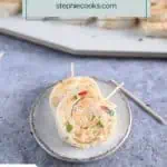 Two pimento cheese pinwheels on a small ceramic plate. A platter of the pinwheels is visible in the background. Text overlay includes recipe name.