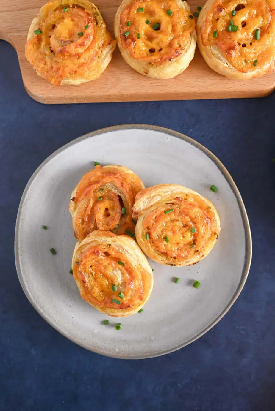 Overhead view of a gray plate holding three hot ham and cheese pinwheels set next to a wooden board holding more pinwheels.