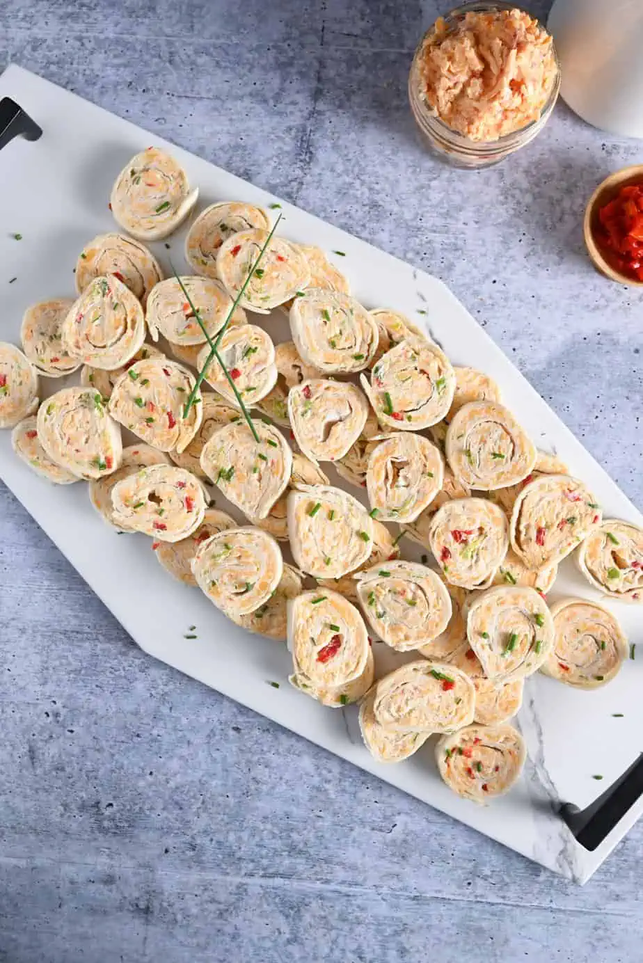 Overhead view of pimento cheese pinwheels lined up on a white tile platter.