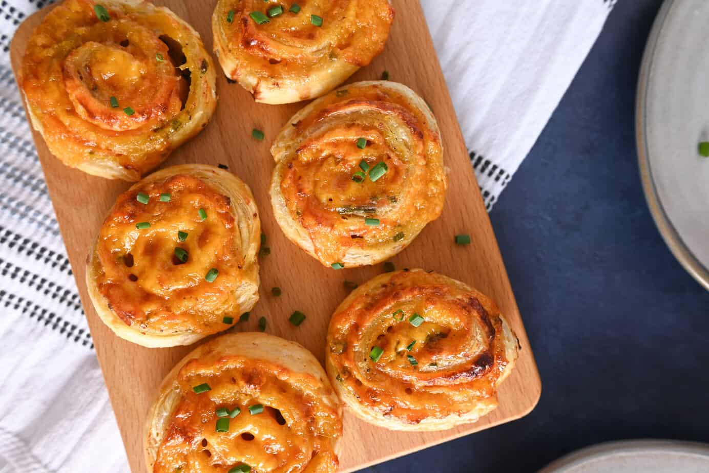 Six hot ham and cheese pinwheels on a wooden serving board.