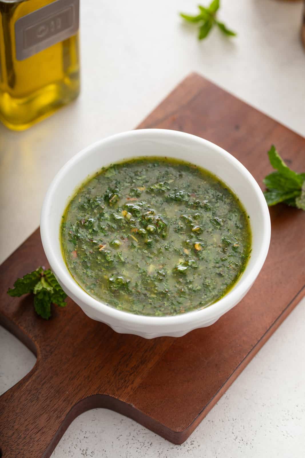 Mint chimichurri in a white bowl set on a wooden board.