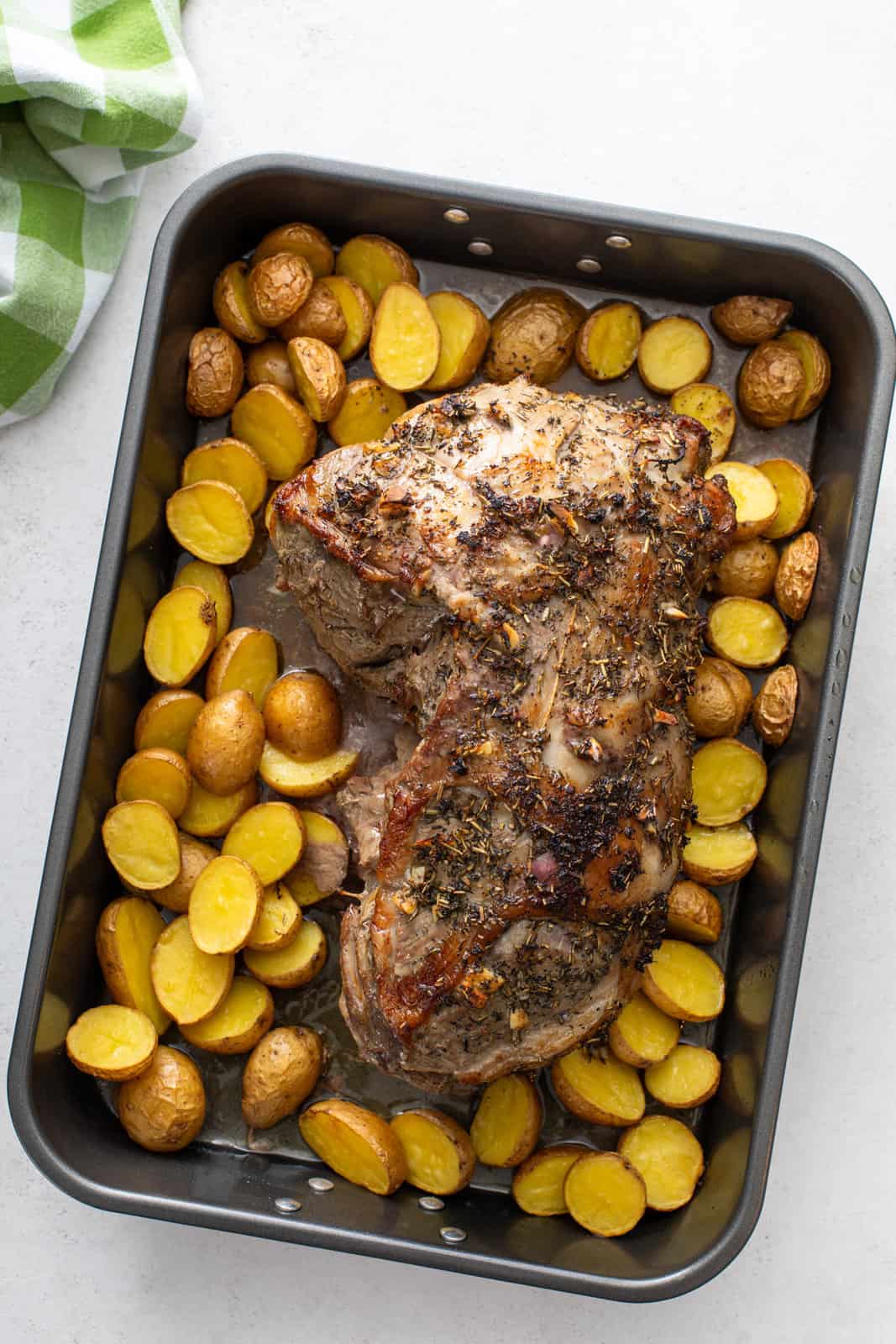 Cooked boneless leg of lamb in a roasting pan surrounded by roasted potatoes.