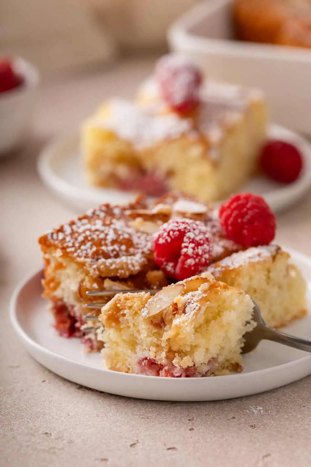 Fork cutting a bite from the corner of a piece of raspberry coffee cake on a white plate.