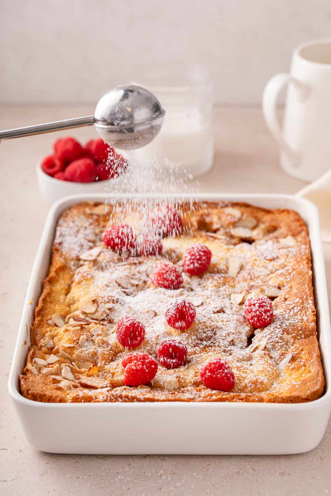 Powdered sugar being dusted over the top of a cooled raspberry coffee cake.