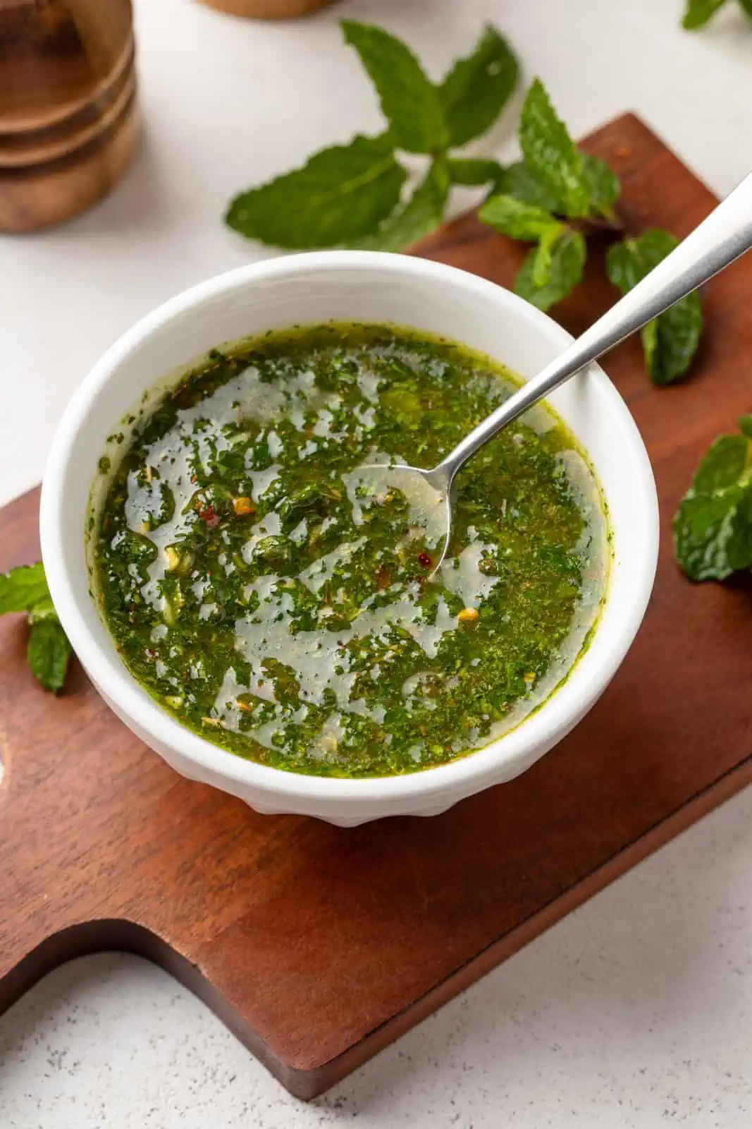 Fresh mint chimichurri in a white bowl with a spoon in it.