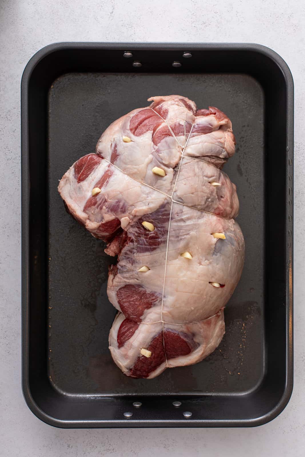 Boneless leg of lamb in a roasting pan, with garlic cloves inserted into the meat.