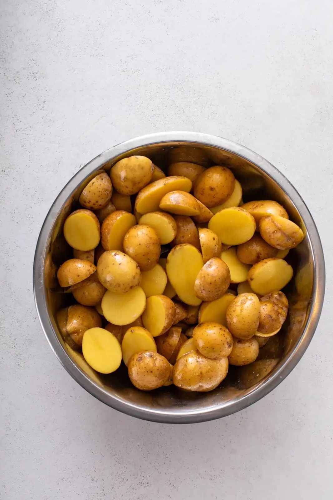 Halved roasting potatoes in a metal mixing bowl.