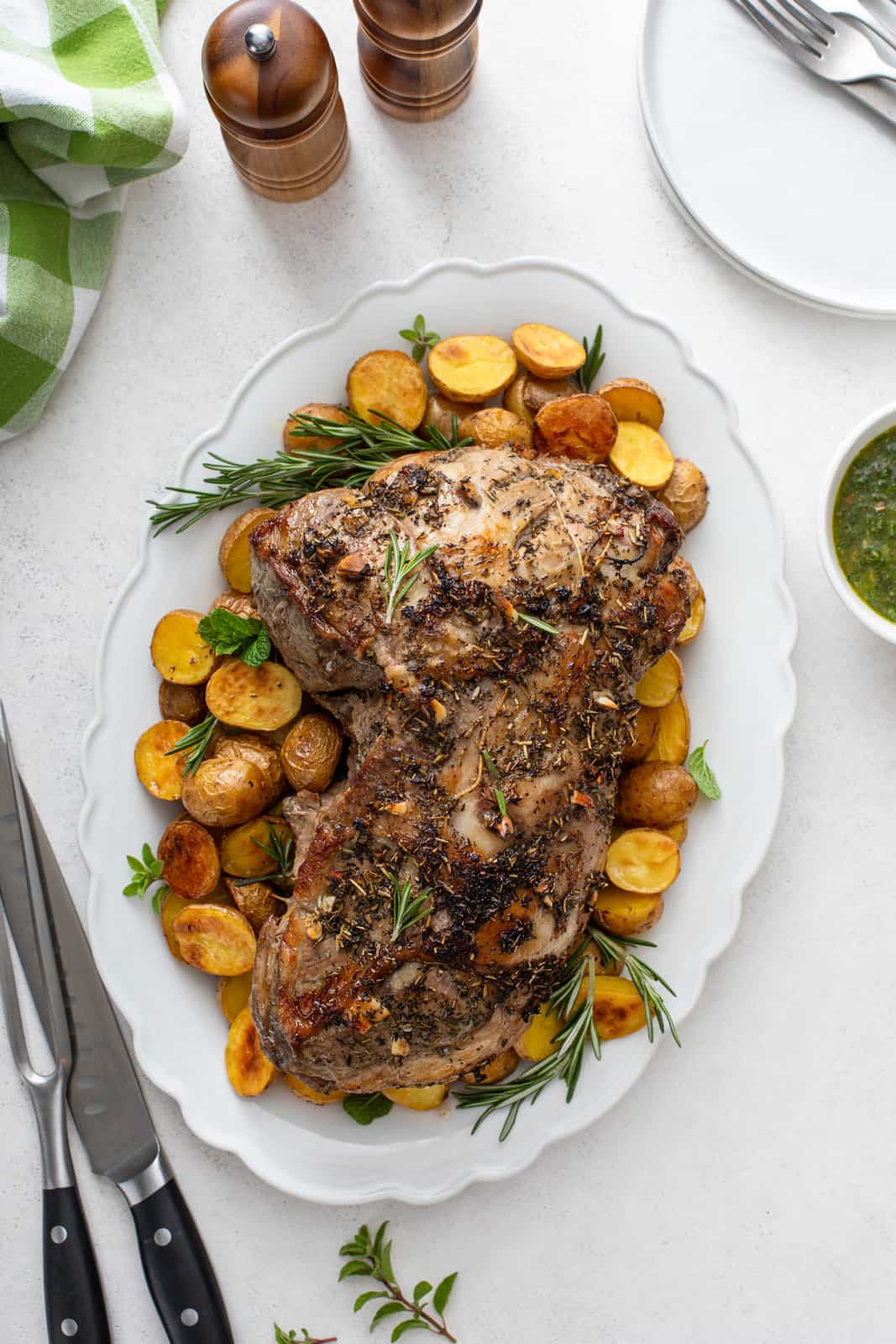 Overhead view of roasted boneless leg of lamb surrounded by roasted potatoes on a white platter.