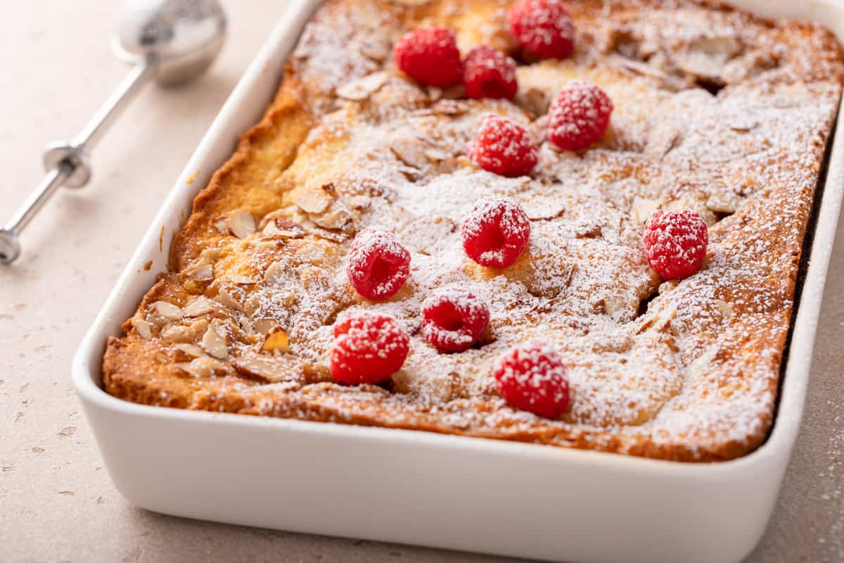 Raspberry almond coffee cake in a white cake pan, dusted with powdered sugar.