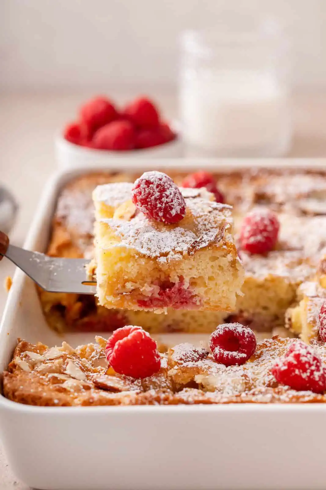 Cake server lifting a slice of raspberry almond coffee cake out of a cake pan.