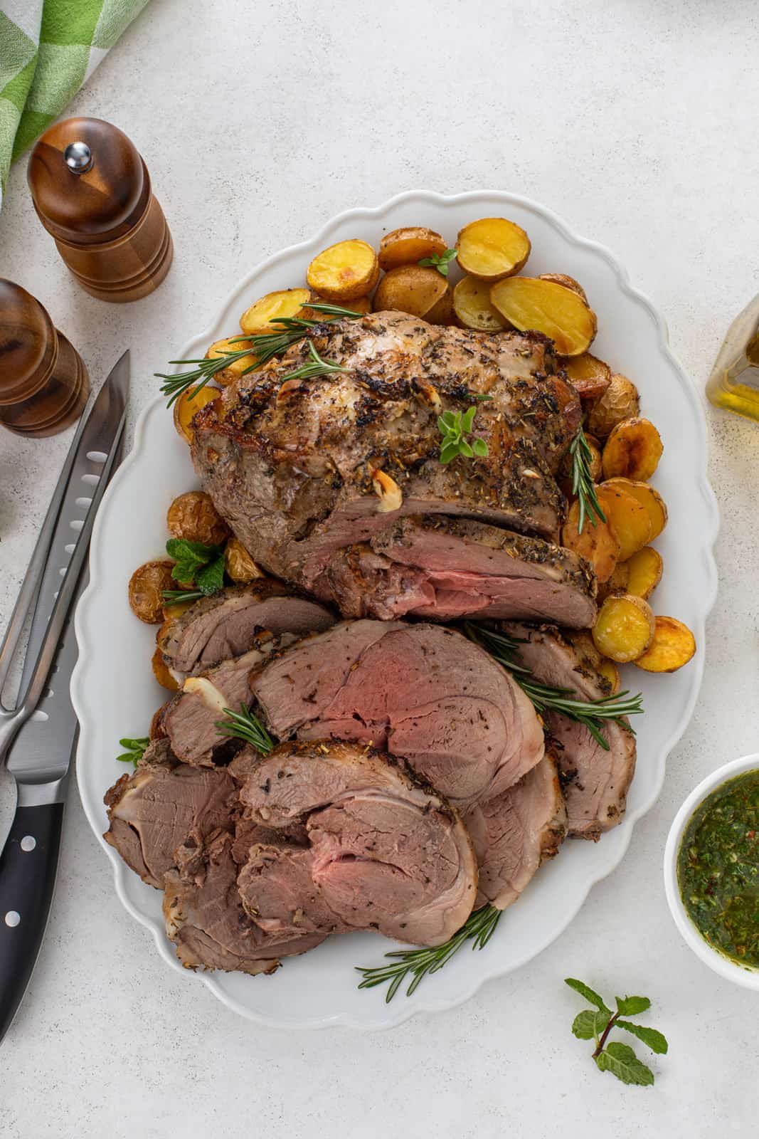Overhead view of sliced roasted boneless leg of lamb on a platter, surrounded by roasted potatoes.