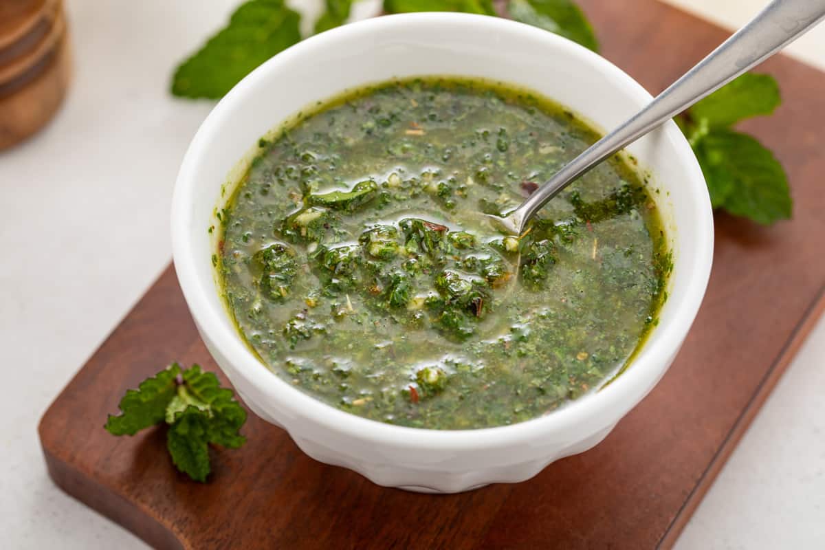 Close up of a spoon in a bowl of mint chimichurri.