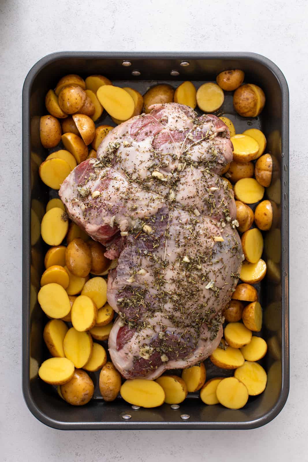 Boneless leg of lamb surrounded by potatoes in a roasting pan, ready to go in the oven.