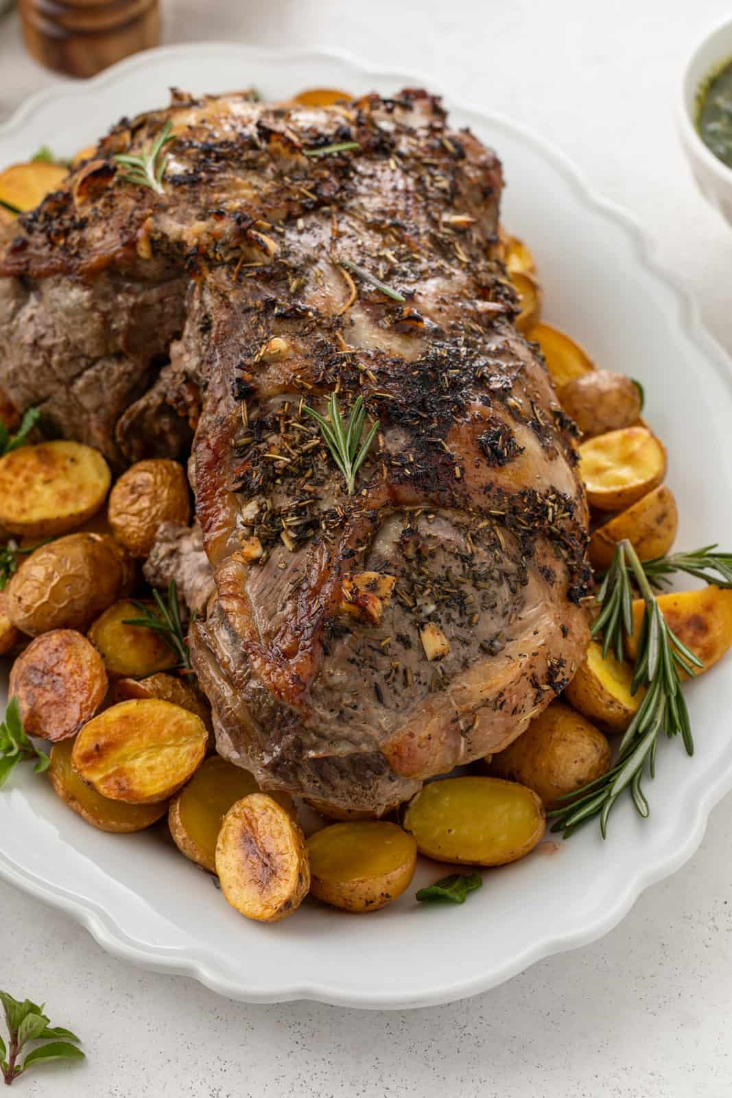 Roasted boneless leg of lamb surrounded by roasted potatoes on a white platter.