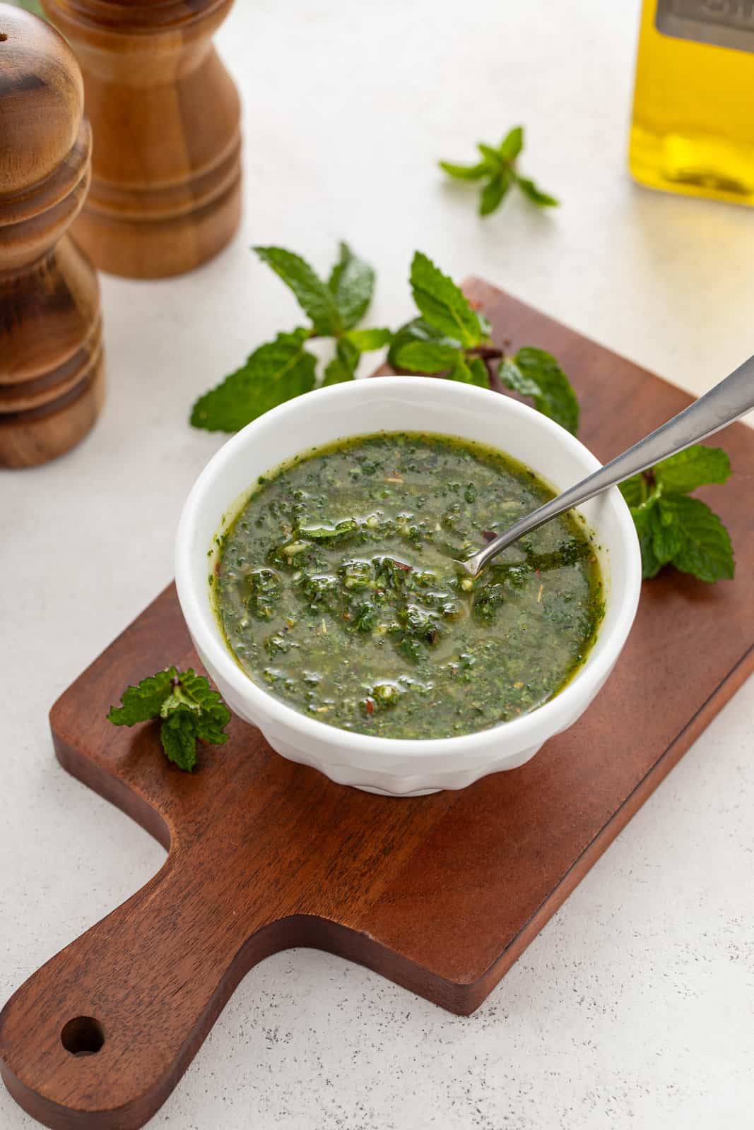 White bowl holding mint chimichurri on a wooden board.