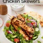 Bowl of salad topped with yogurt-marinated chicken skewers. Text overlay includes recipe name.