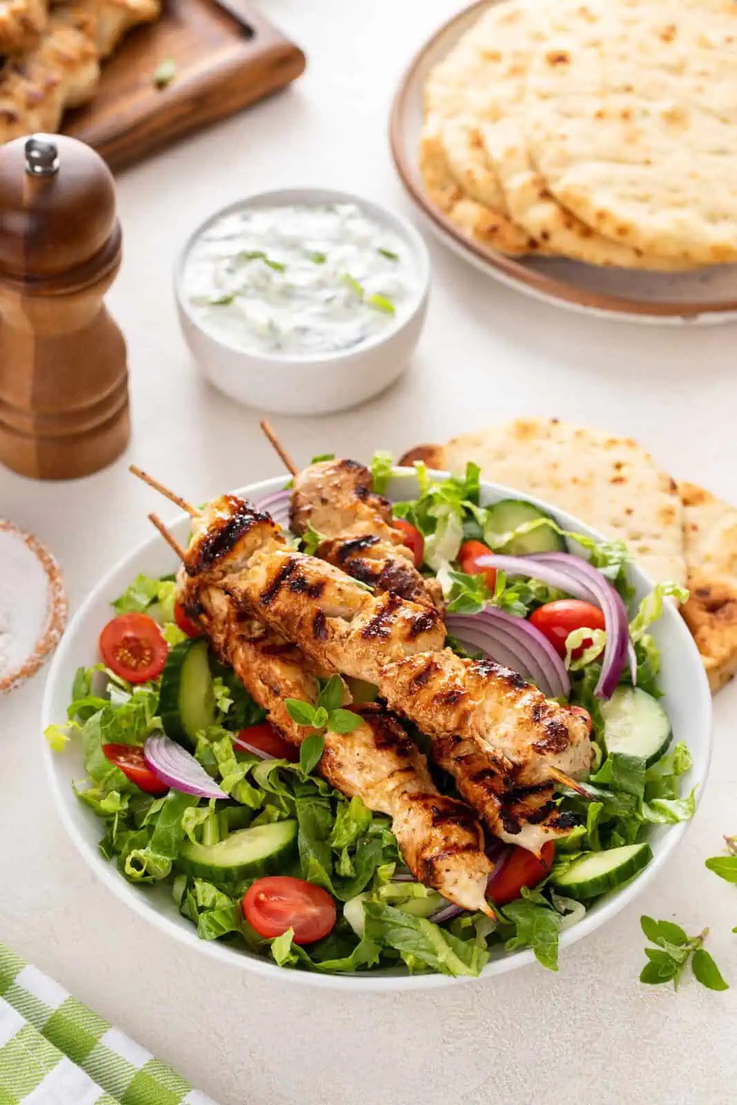 Bowl of salad topped with yogurt-marinated chicken skewers.