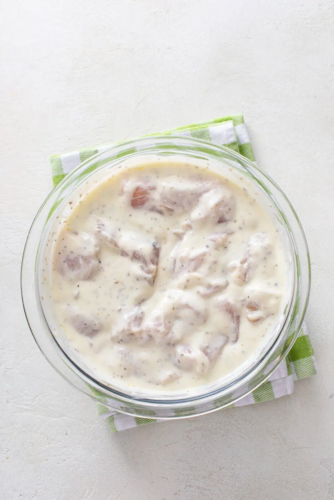 Pieces of chicken in yogurt marinade in a glass bowl.