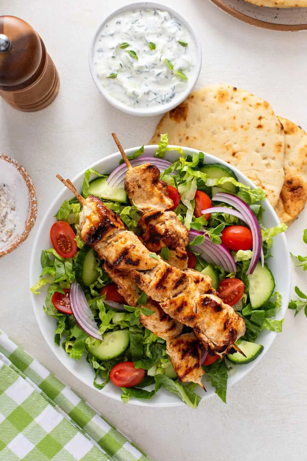 Overhead view of three grilled chicken skewers arranged on top of a green salad.