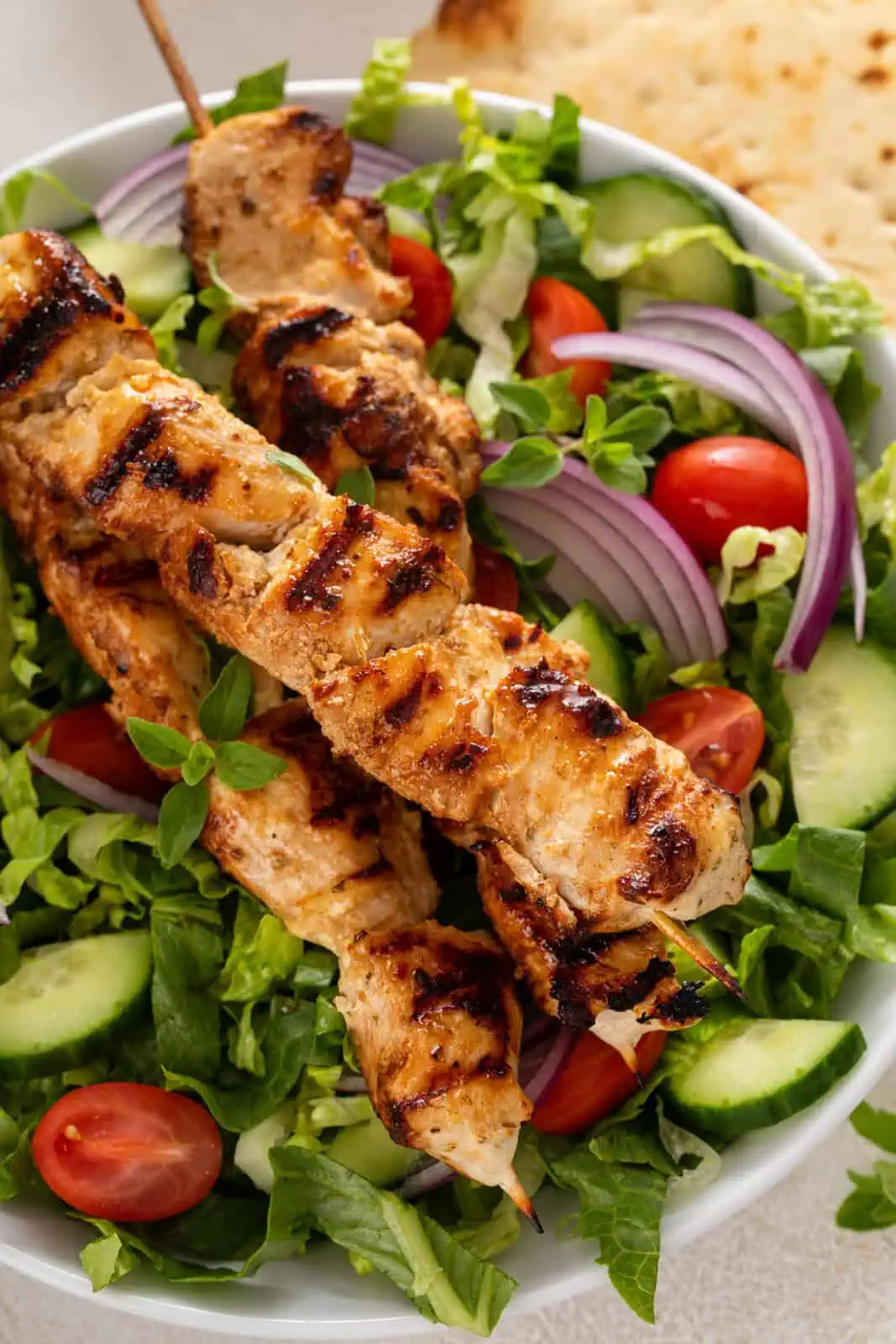 Close up of yogurt-marinated chicken skewers on top of a green salad.