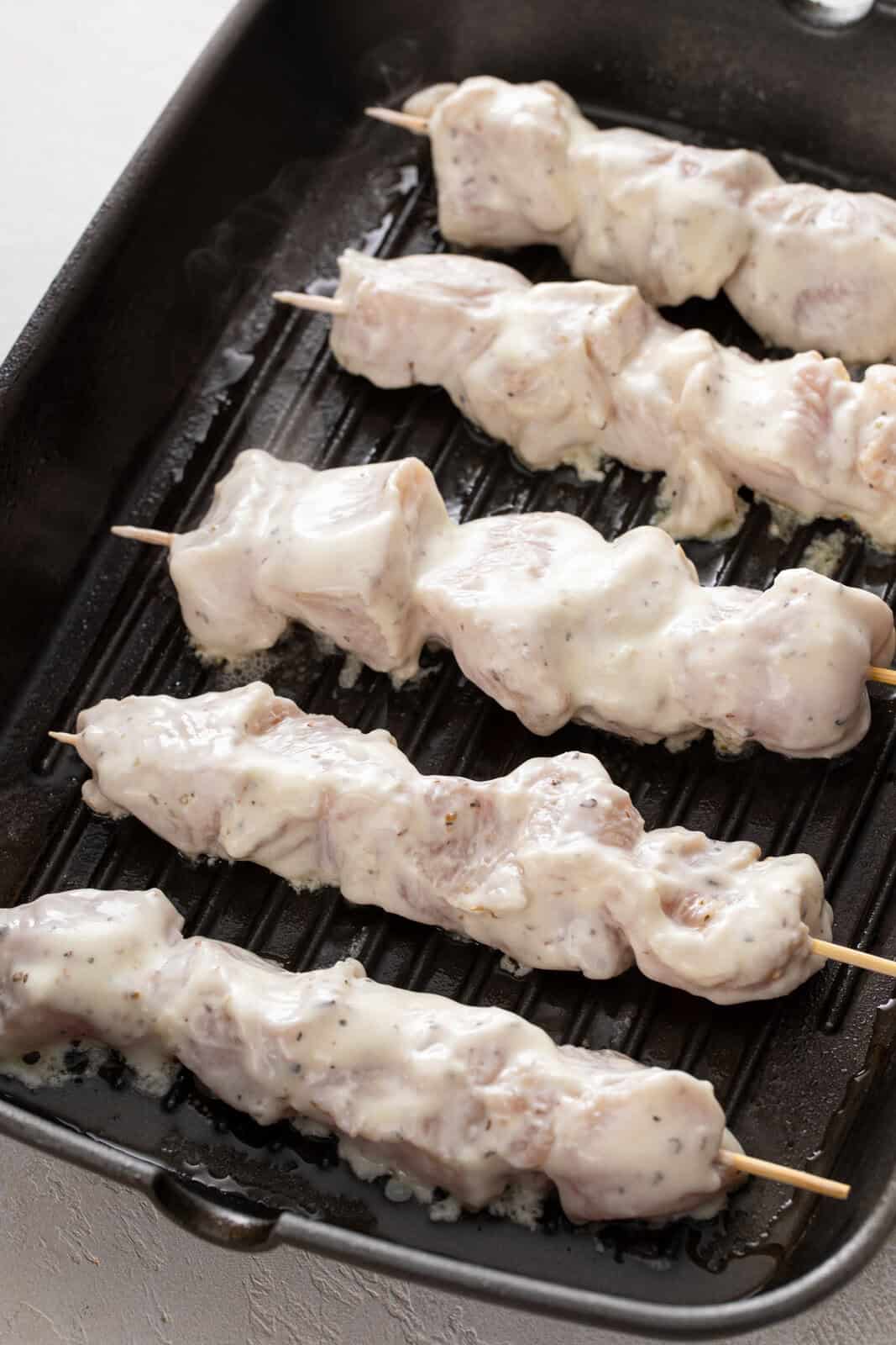 Yogurt-marinated chicken pieces on wooden skewers over a grill pan.