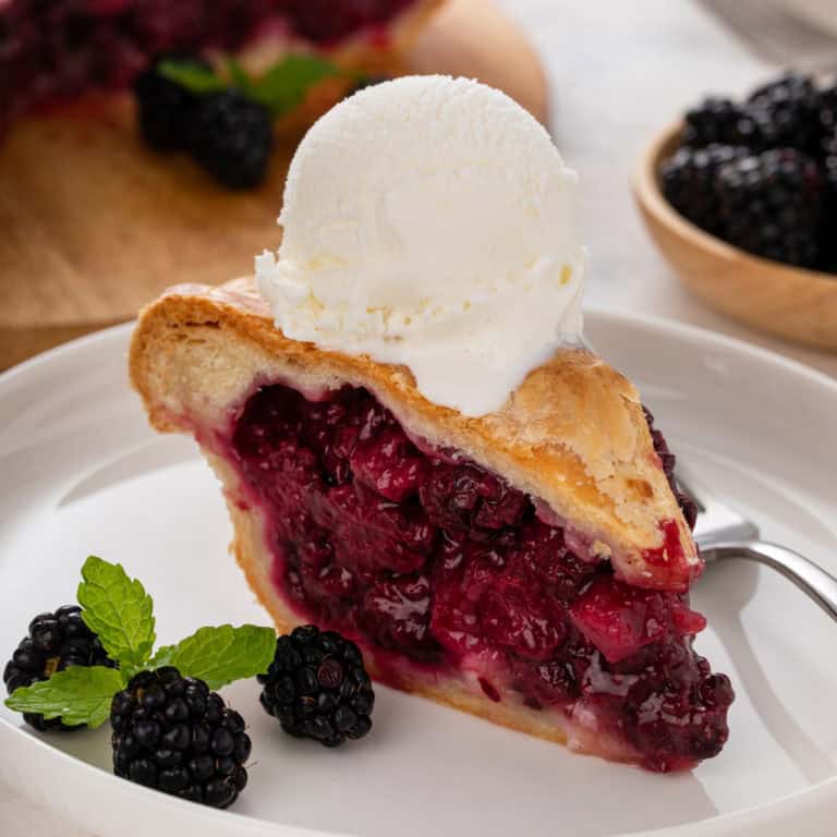 Slice of blackberry pie topped with a scoop of vanilla ice cream.