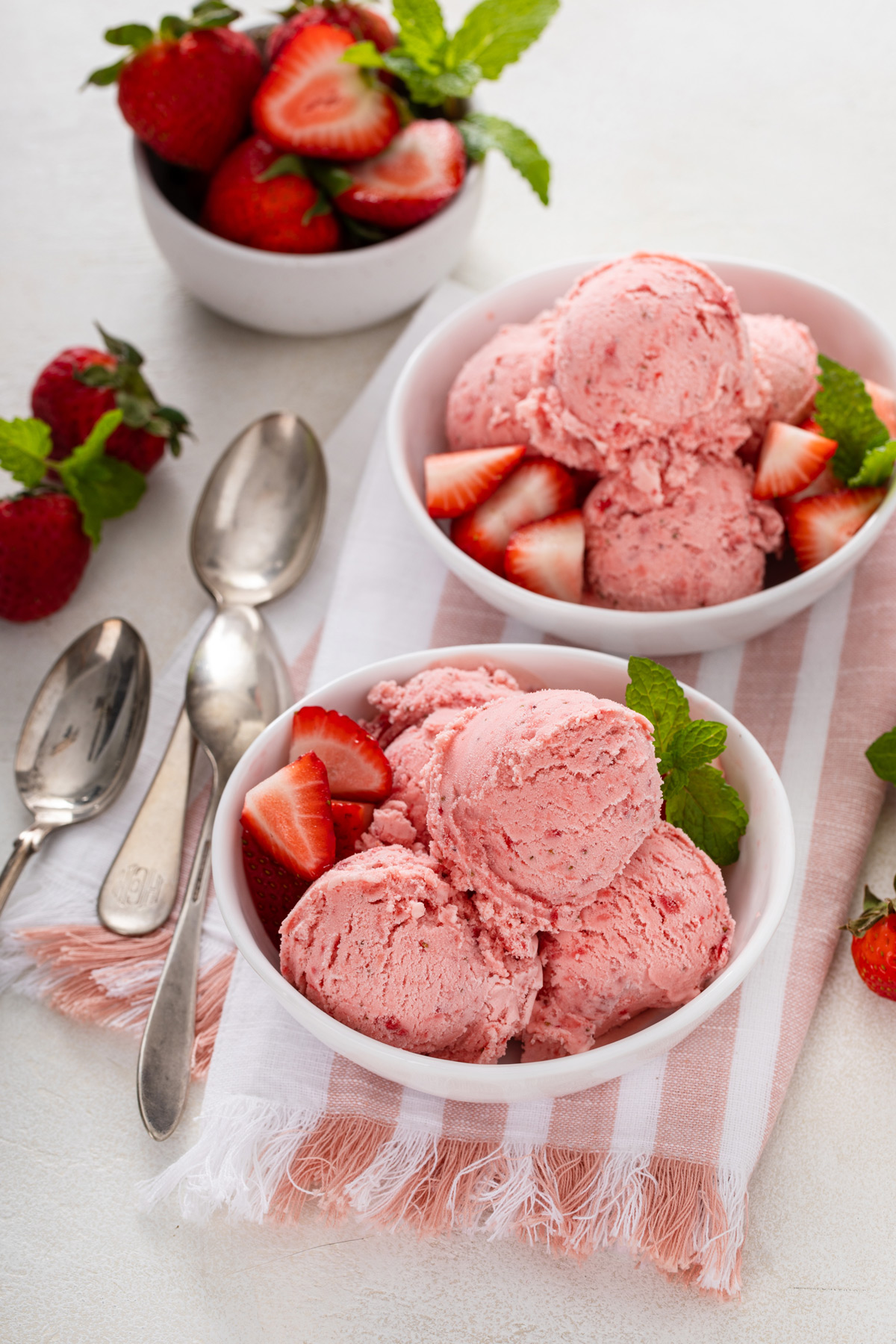 Two white bowls, each filled with several scoops of strawberry ice cream.