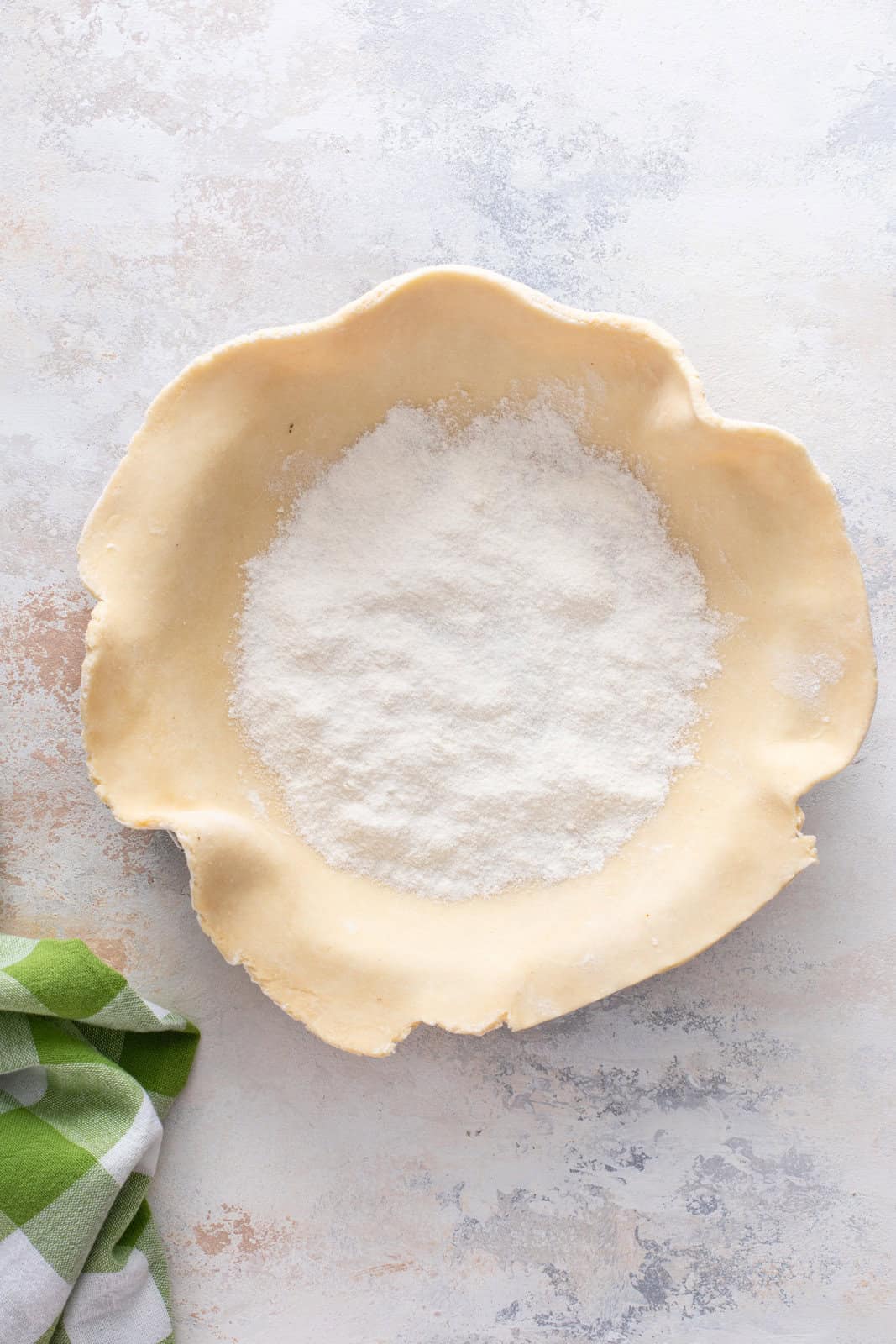 Sugar and flour sprinkled into the bottom of a pie crust in a pie pan.