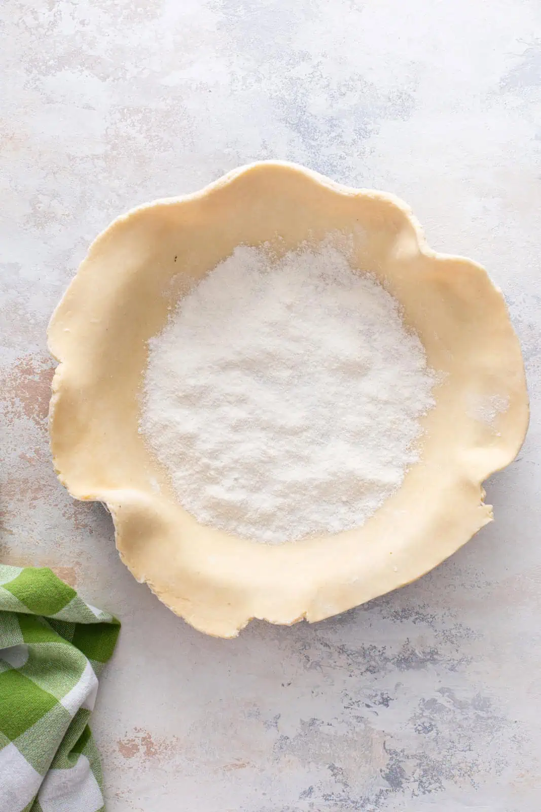Sugar and flour sprinkled into the bottom of a pie crust in a pie pan.