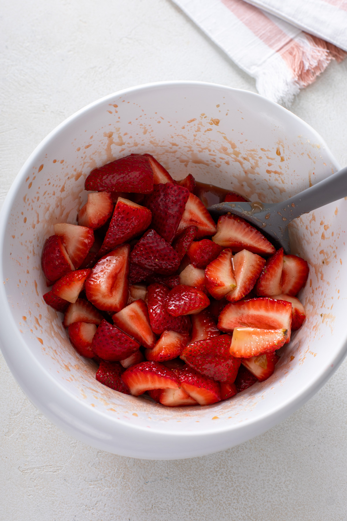 Quartered strawberries macerating in a white bowl.