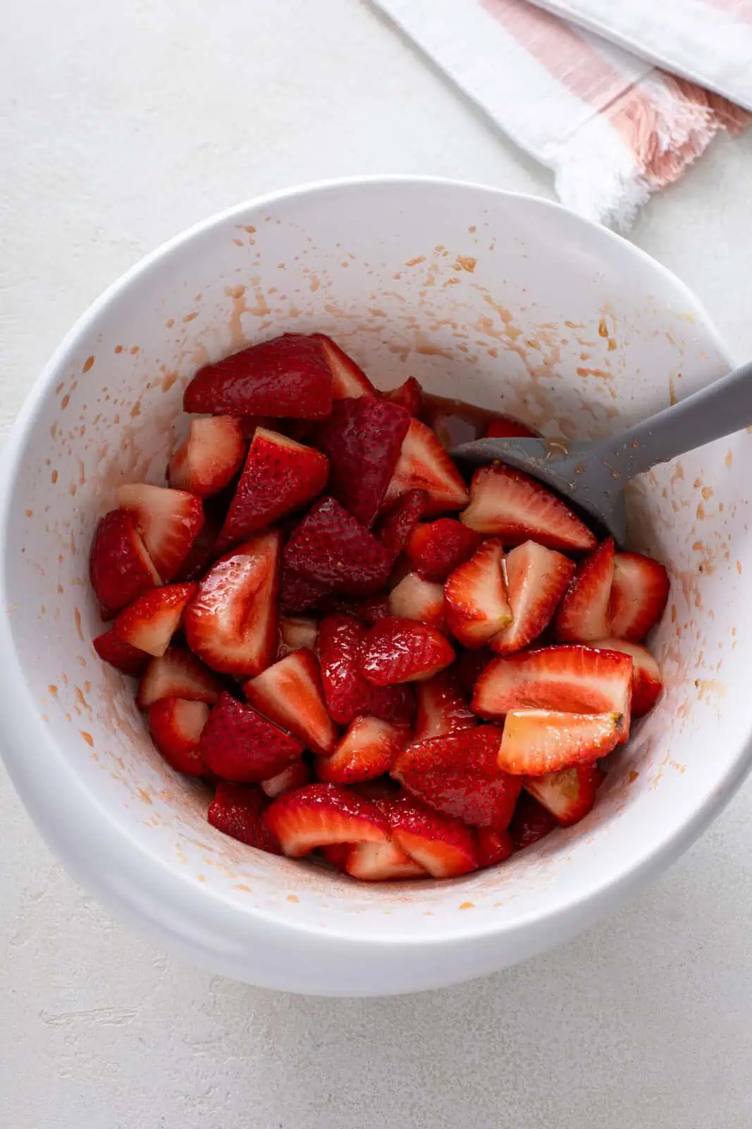 Quartered strawberries macerating in a white bowl.