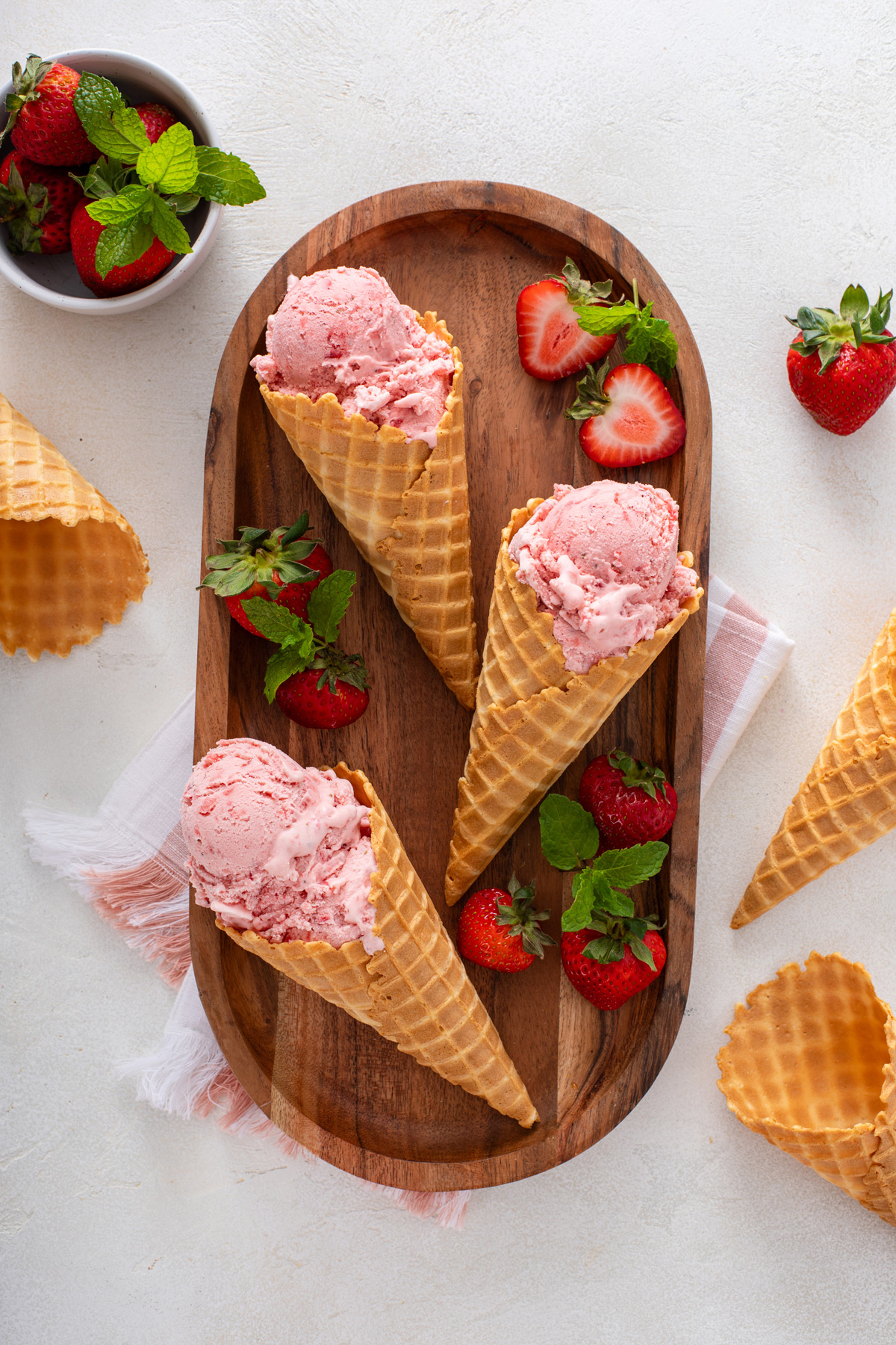 Three waffle cones, each filled with strawberry ice cream, resting on a wooden board.