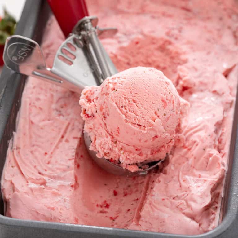 Ice cream scoop scooping up strawberry ice cream from a loaf pan container.