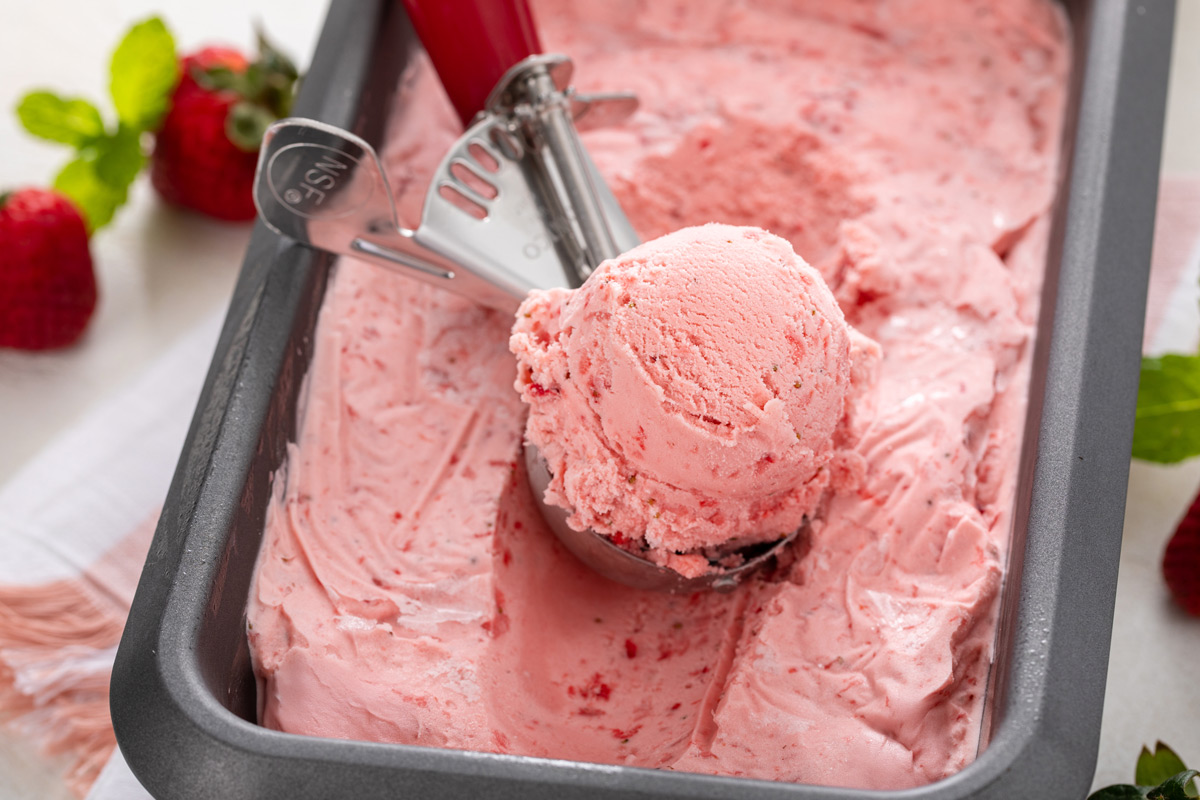 Strawberry ice cream being scooped out of a loaf pan container.