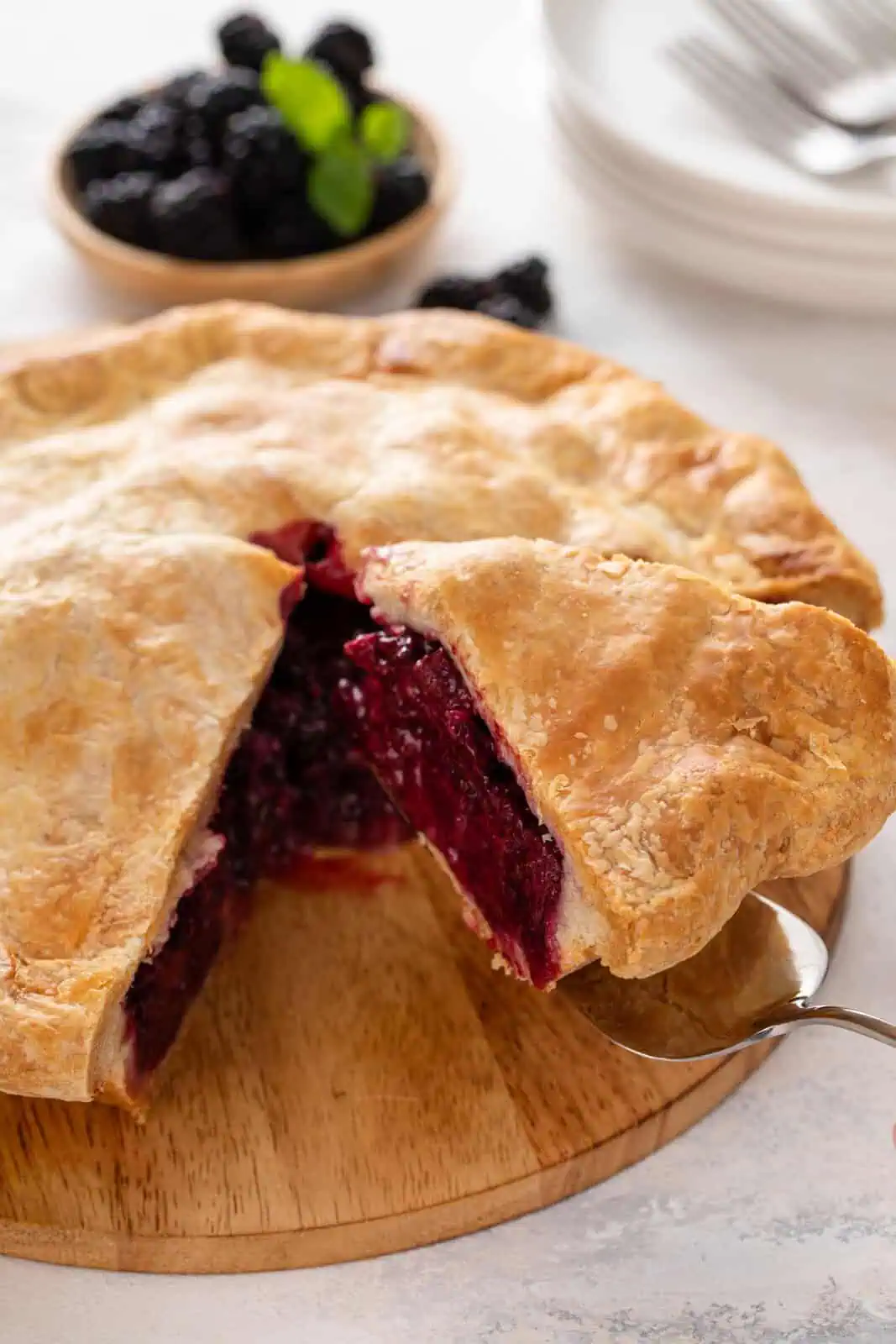 Pie server lifting up a slice of blackberry pie from a wooden board.