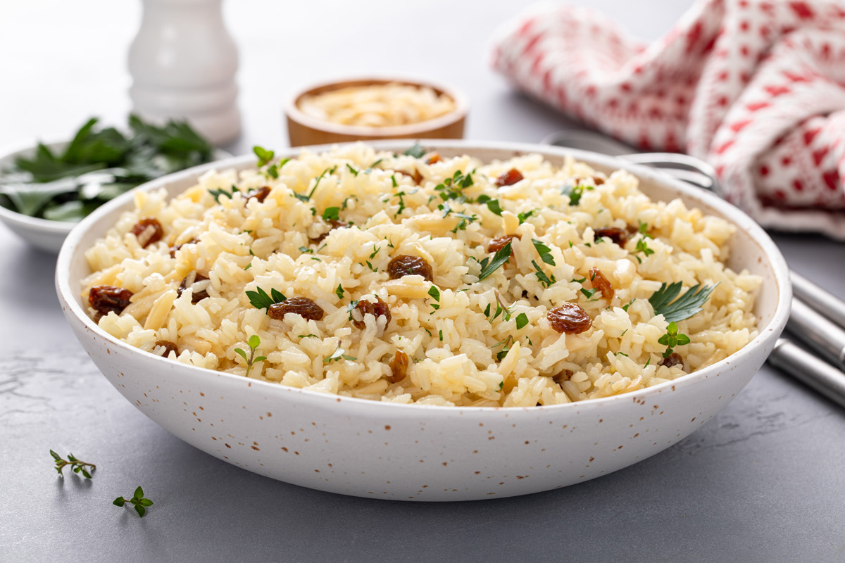 Side view of a white serving bowl filled with almond rice pilaf.