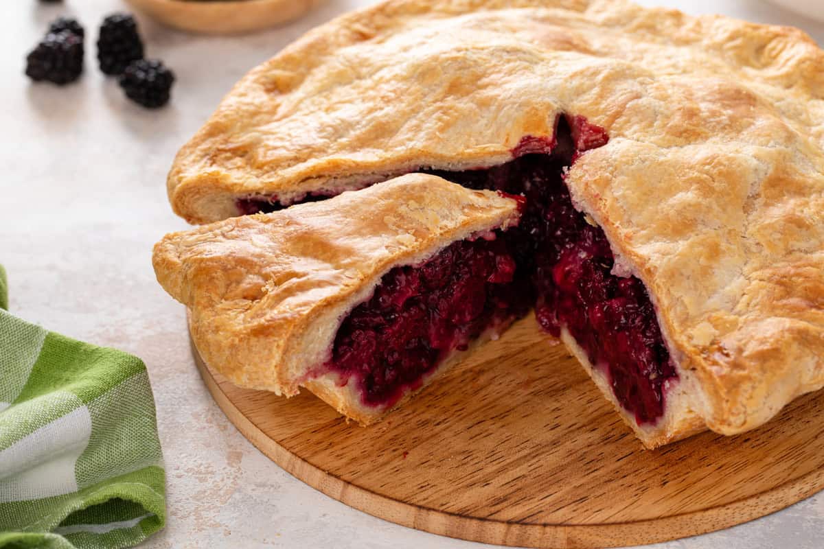 Sliced blackberry pie on a wooden board.