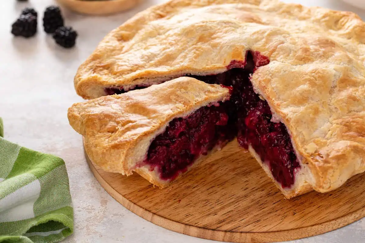 Sliced blackberry pie on a wooden board.