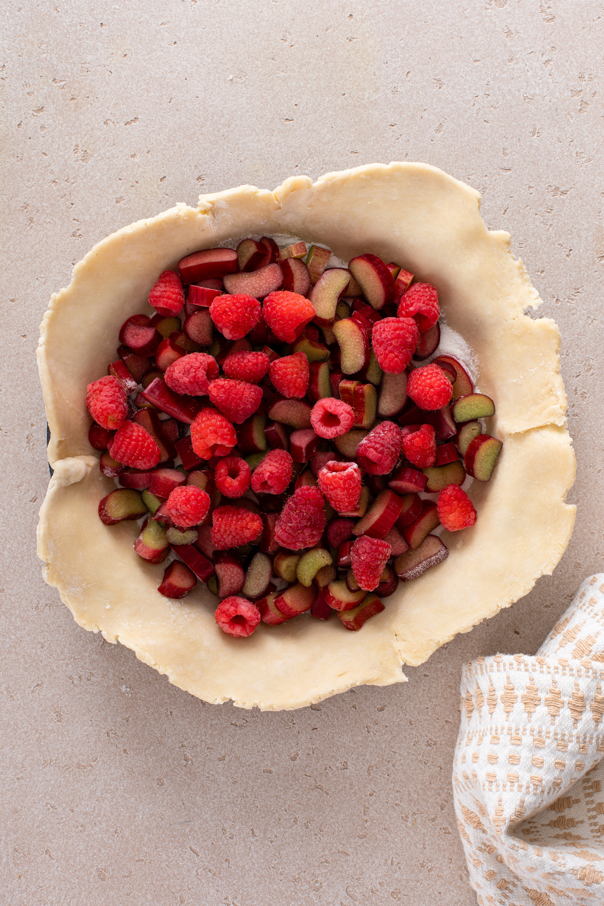 Rhubarb and raspberries being layered in a pie crust.
