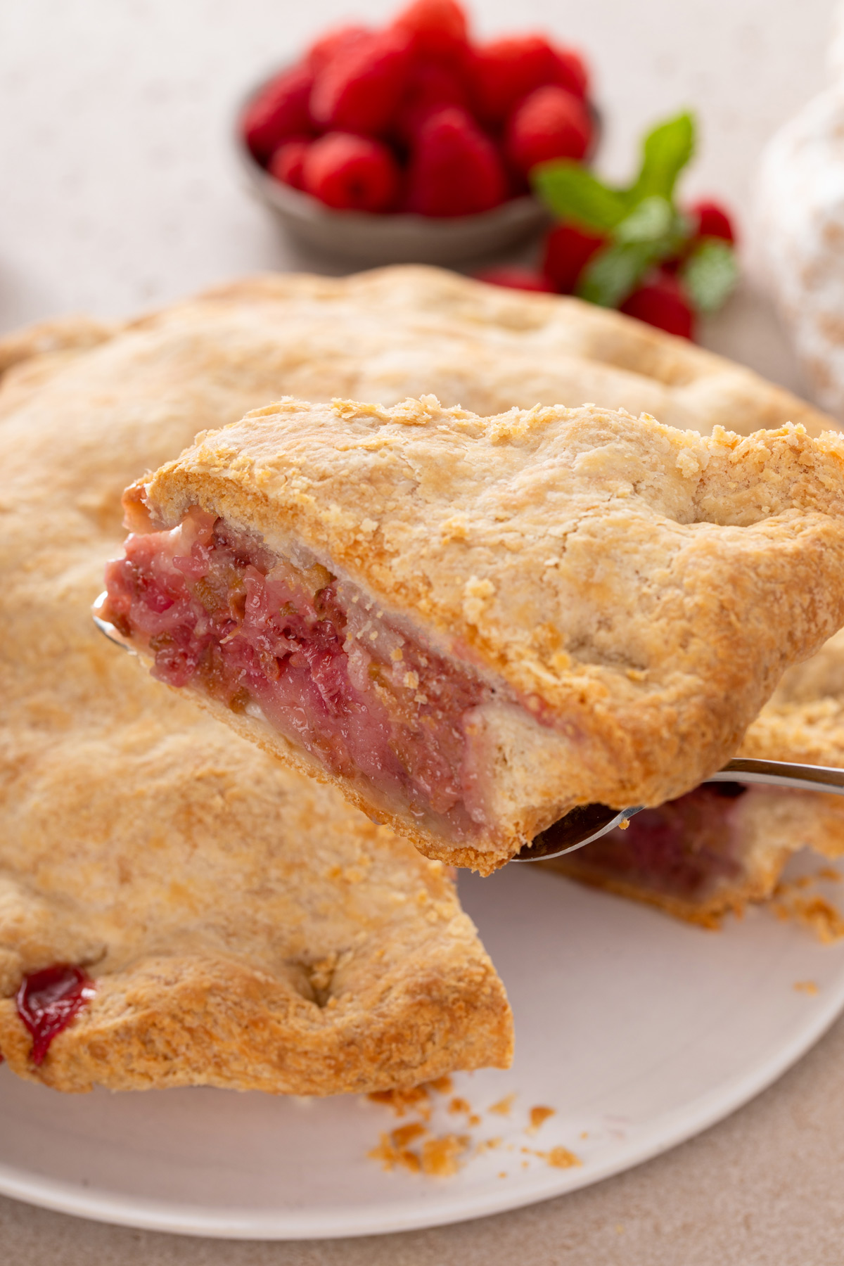Pie server lifting up a slice of raspberry rhubarb pie.