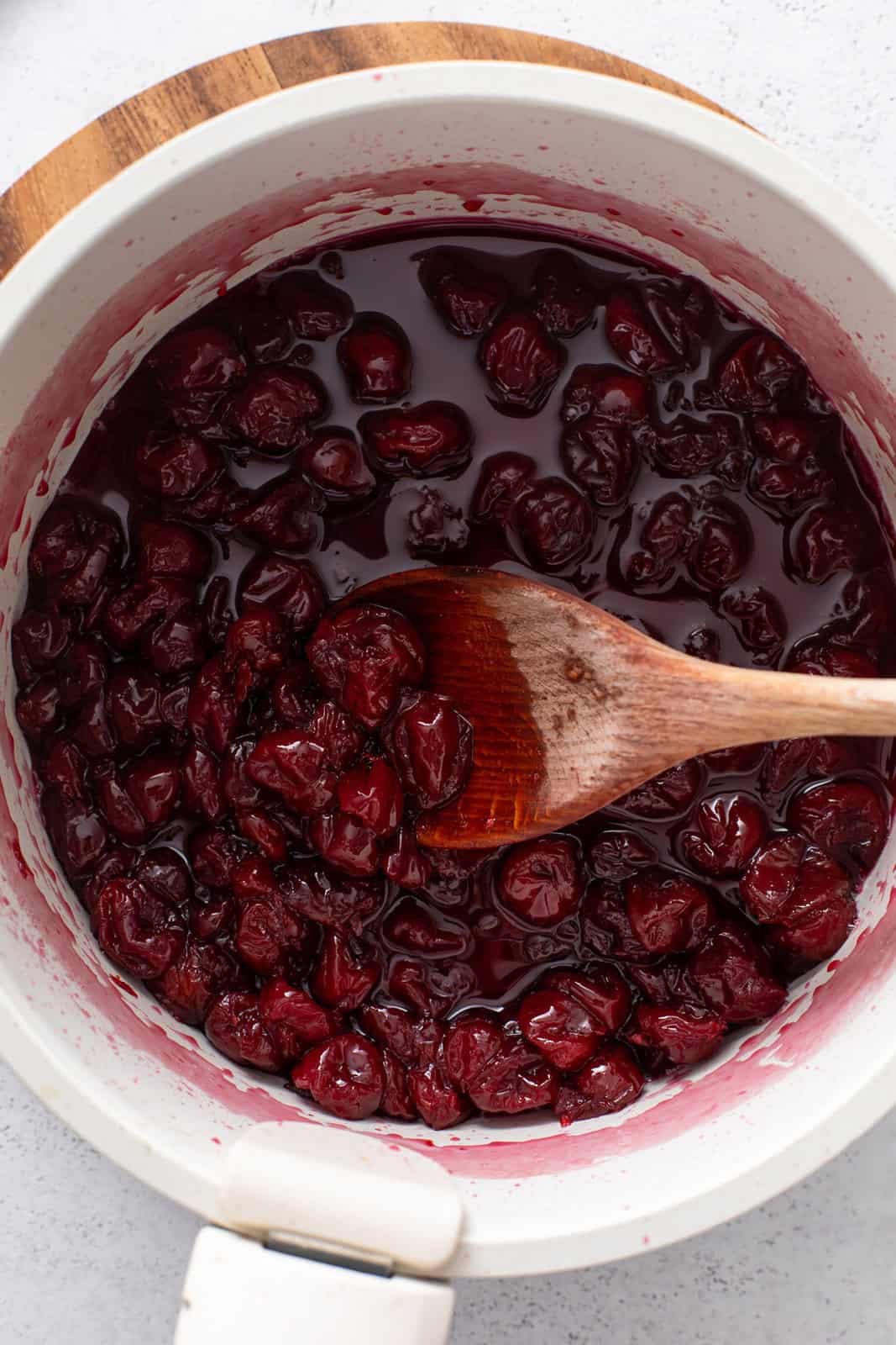 Cherry jam filling cooked down in a white pot.
