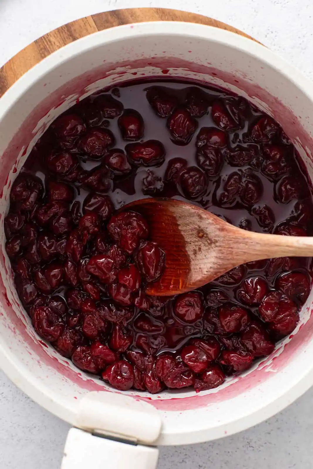Cherry jam filling cooked down in a white pot.