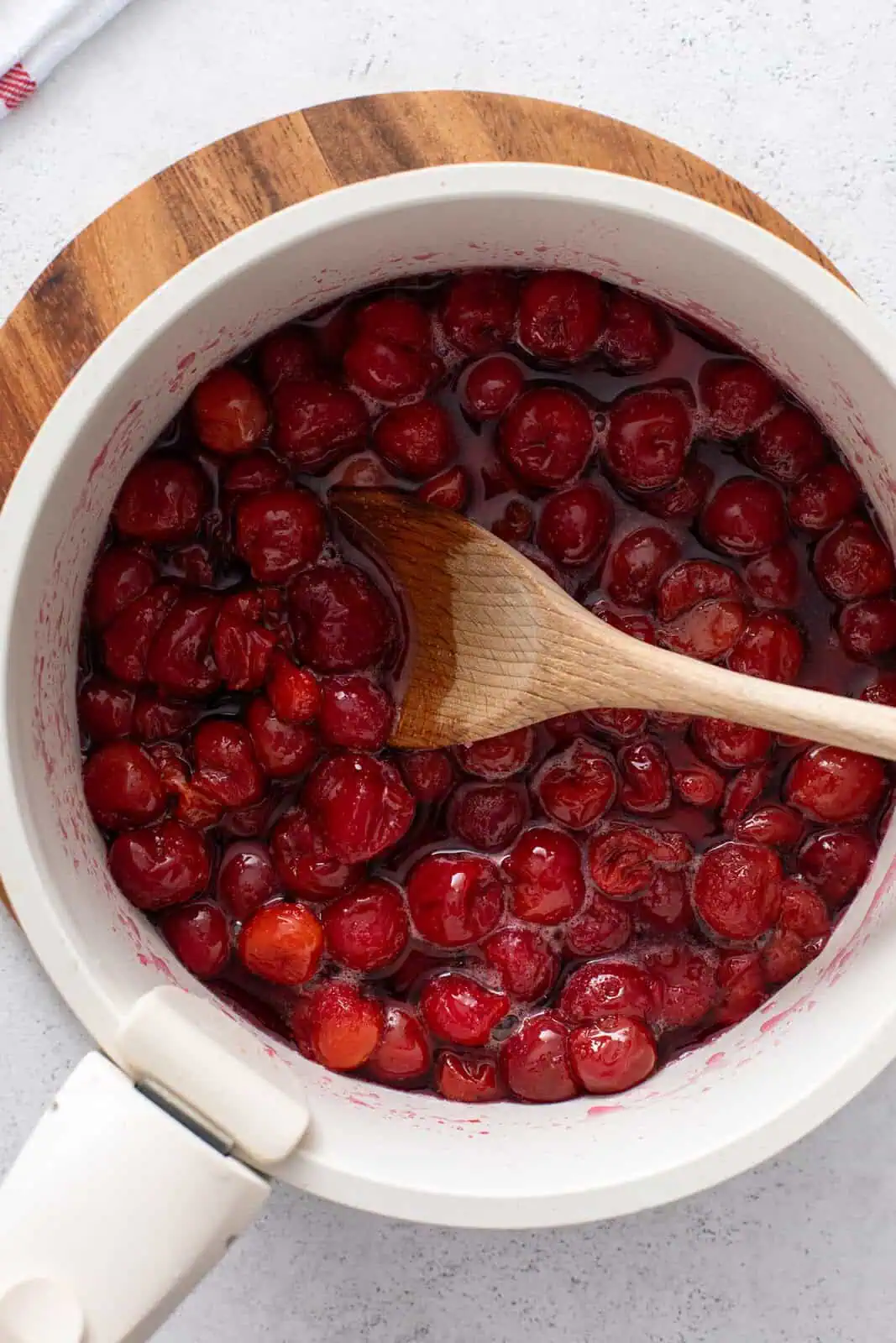 Wooden spoon stirring cherry filling cooking in a pot.