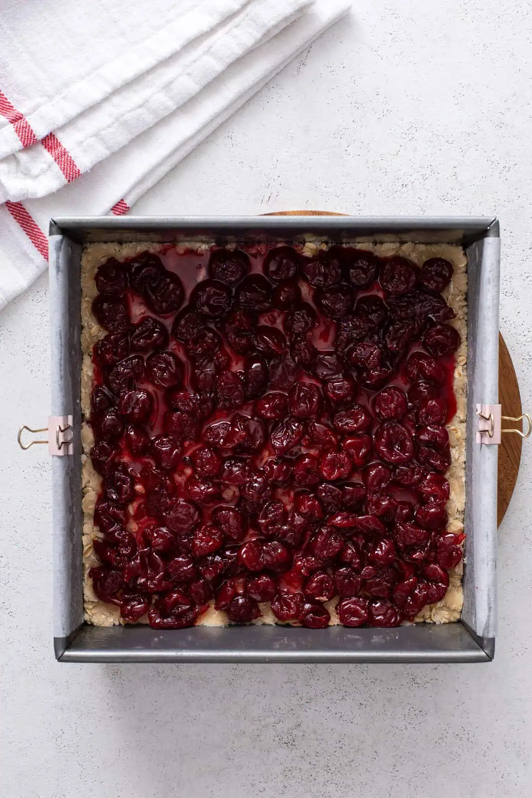 Cherry filling spread over oat crust in a metal pan.