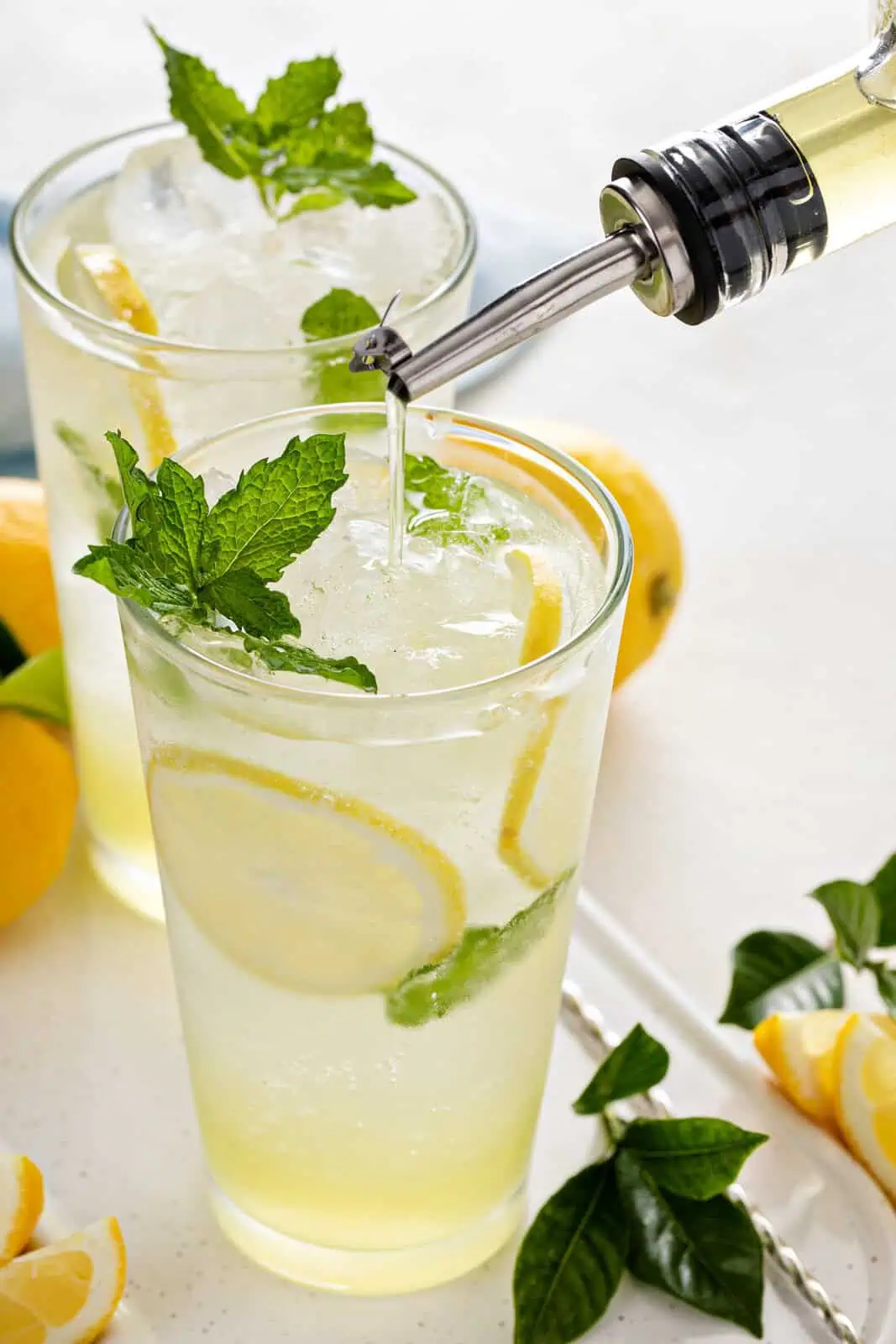 Lemon syrup being poured into a glass of sparkling water garnished with mint and lemon slices.