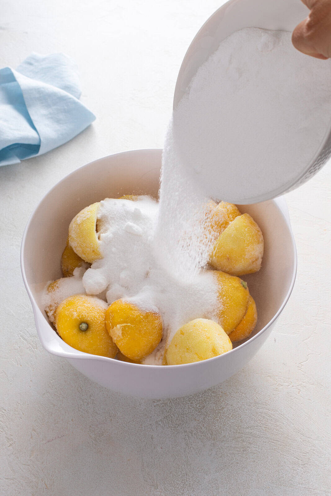 Sugar being added to a bowl of spent lemon rinds.