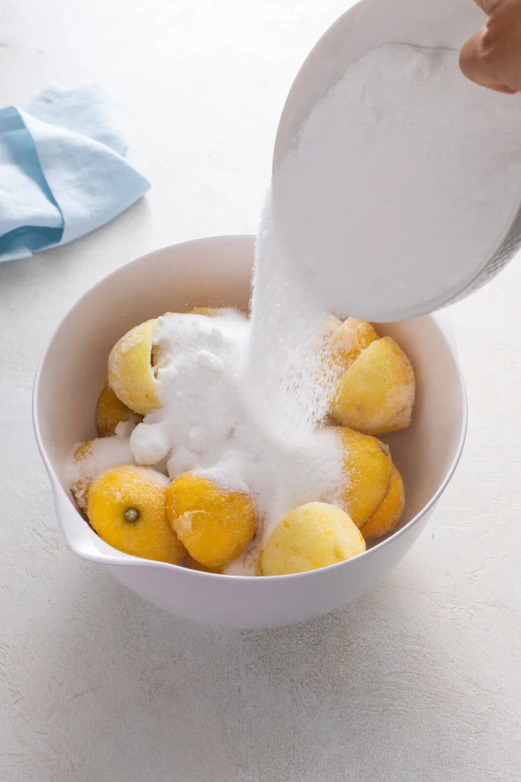Sugar being added to a bowl of spent lemon rinds.
