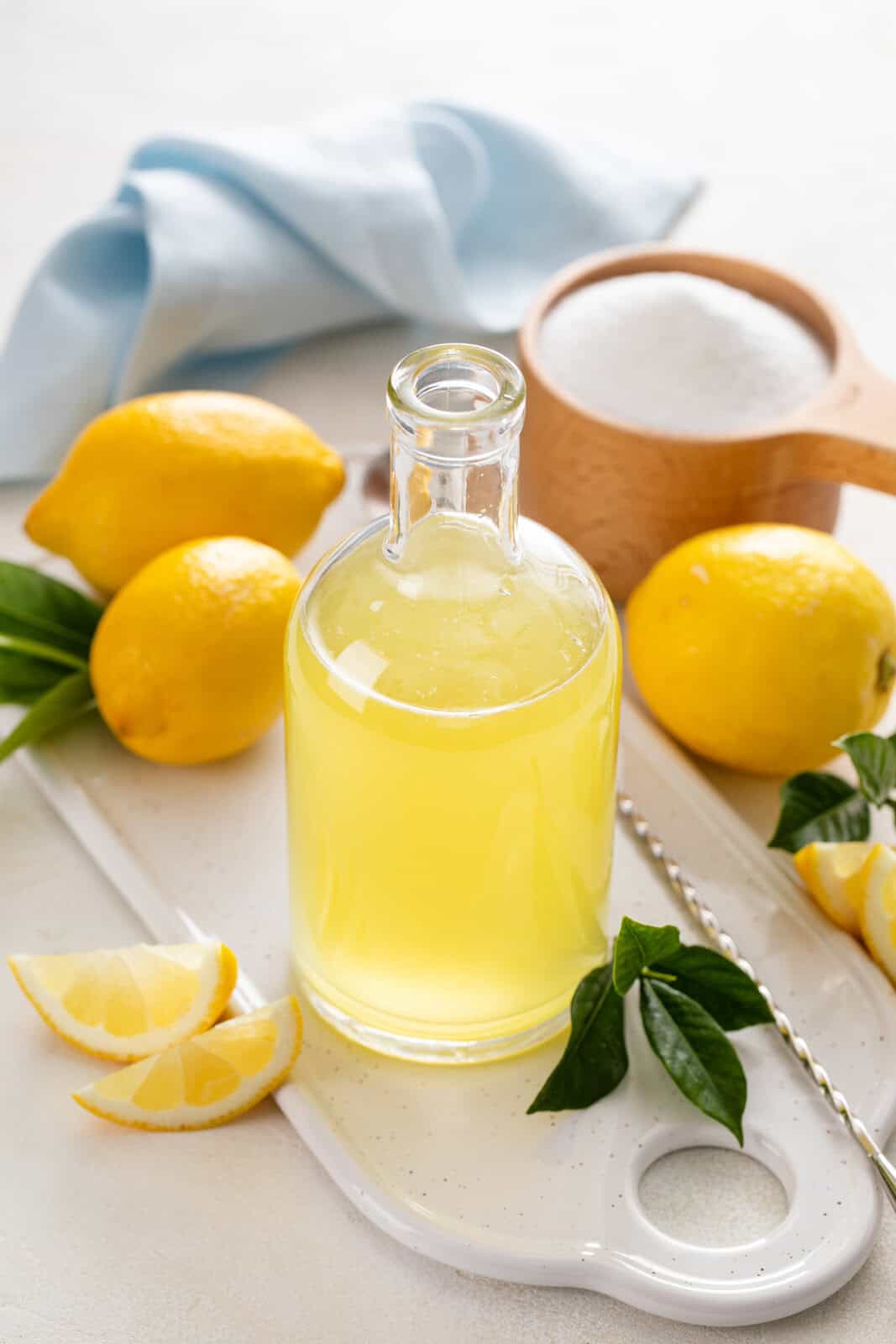 Glass bottle of easy lemon syrup with lemons and sugar in the background.
